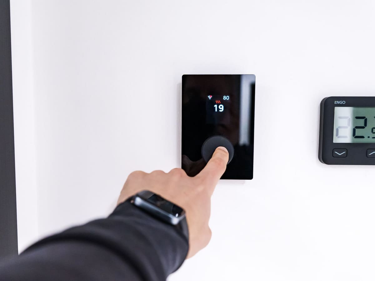 Mano ajustando un termostato digital en la pared de una vivienda